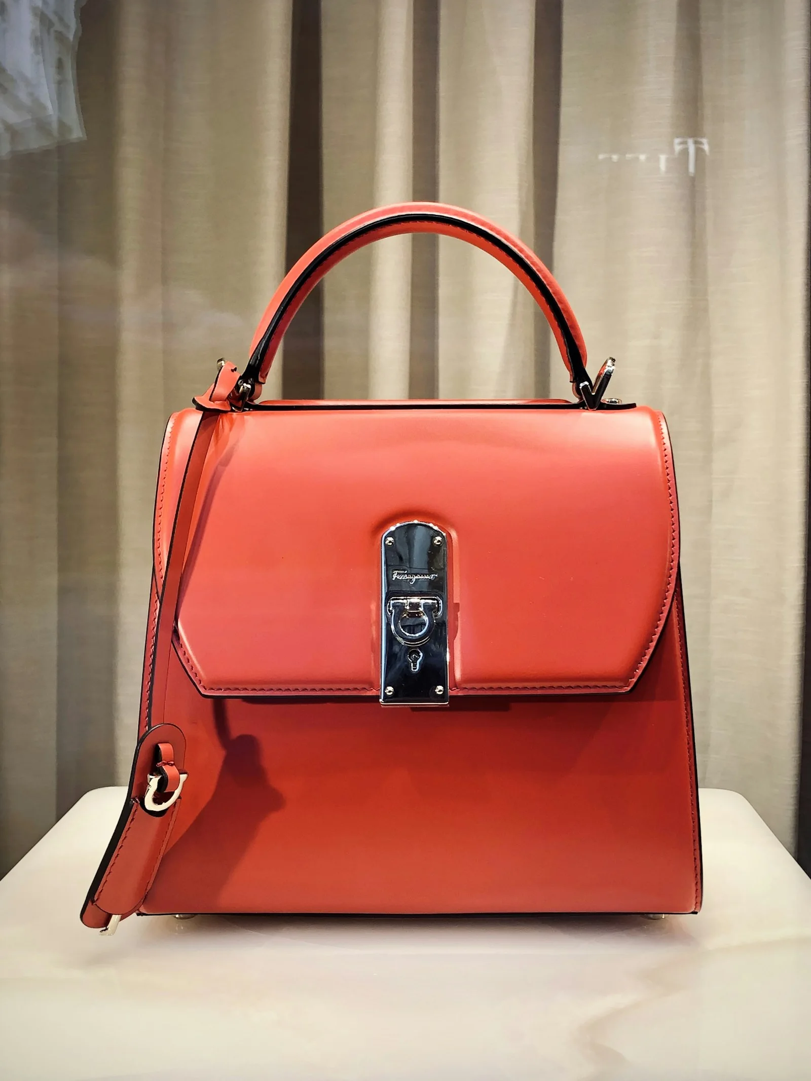 Structured red handbag on a display shelf.