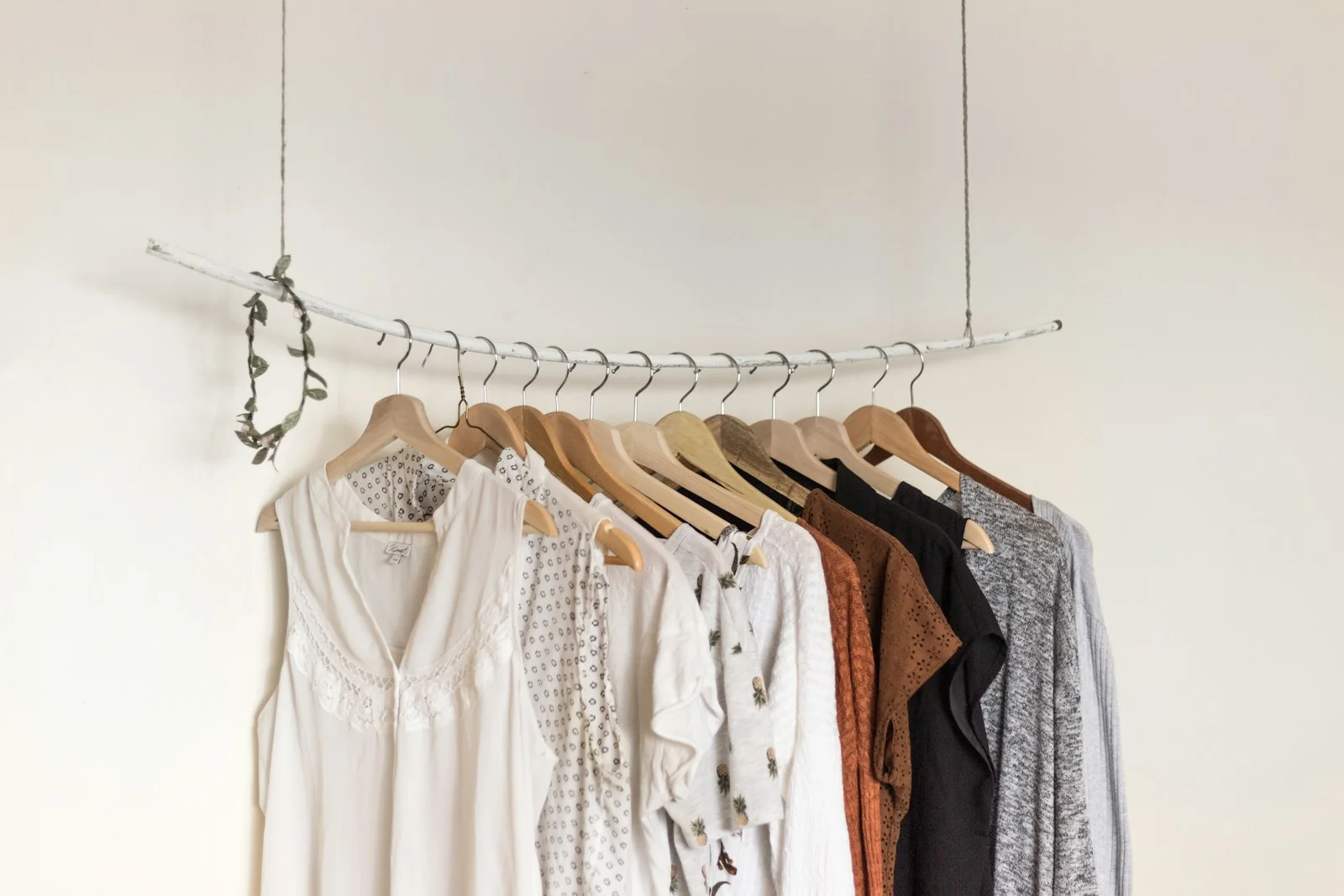 Light and neutral clothes on a simple wooden hanger rail.
