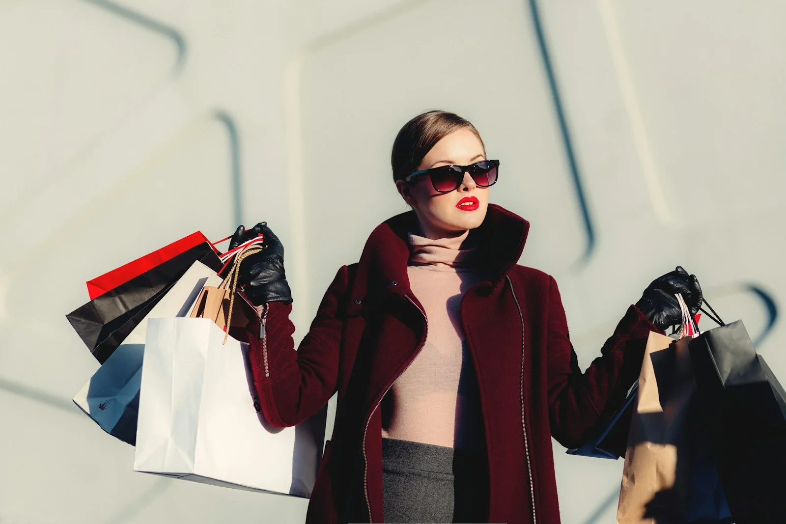 Woman in sunglasses and a burgundy coat holding shopping bags