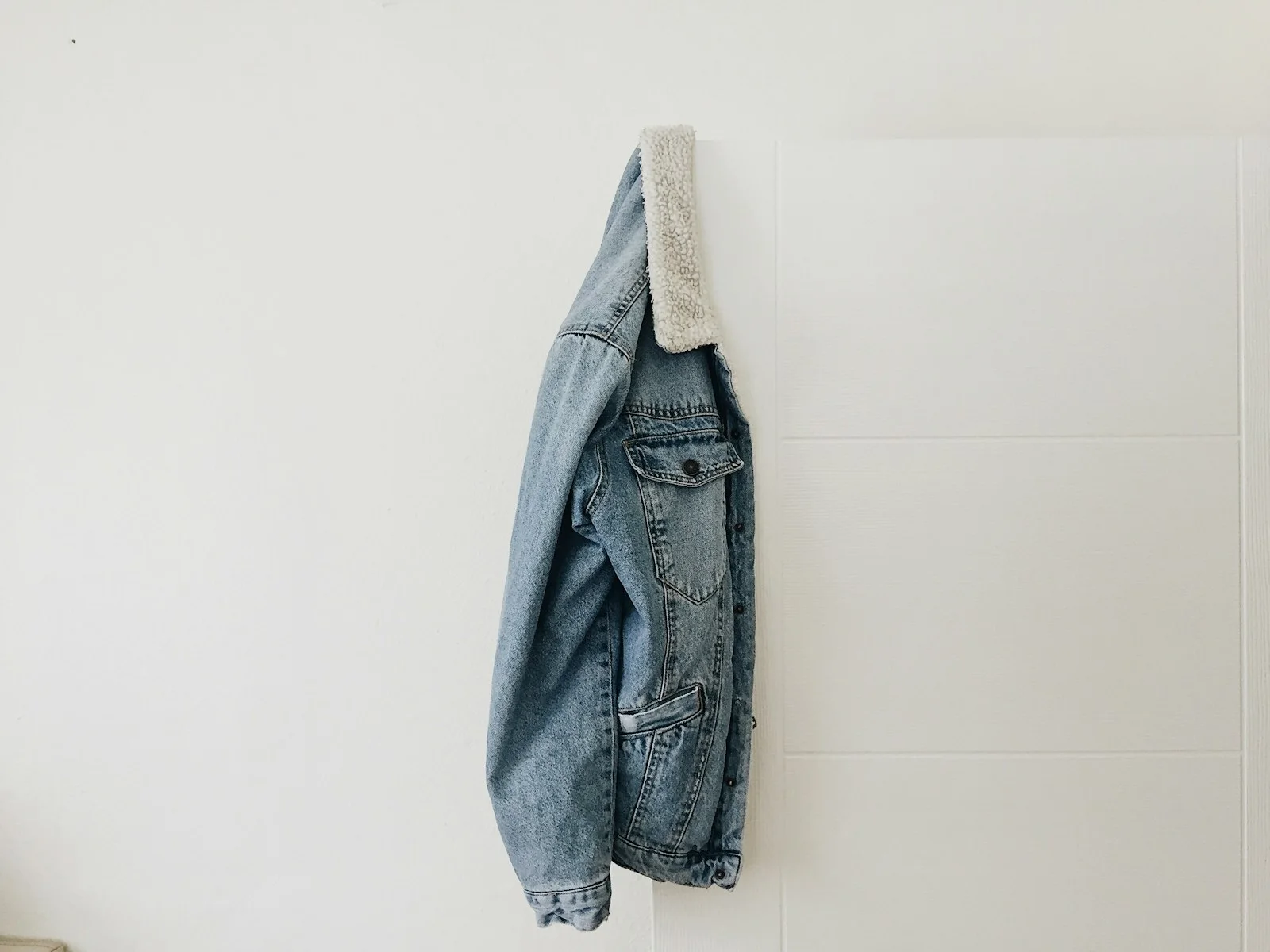 Denim jacket hanging against a pale wall.