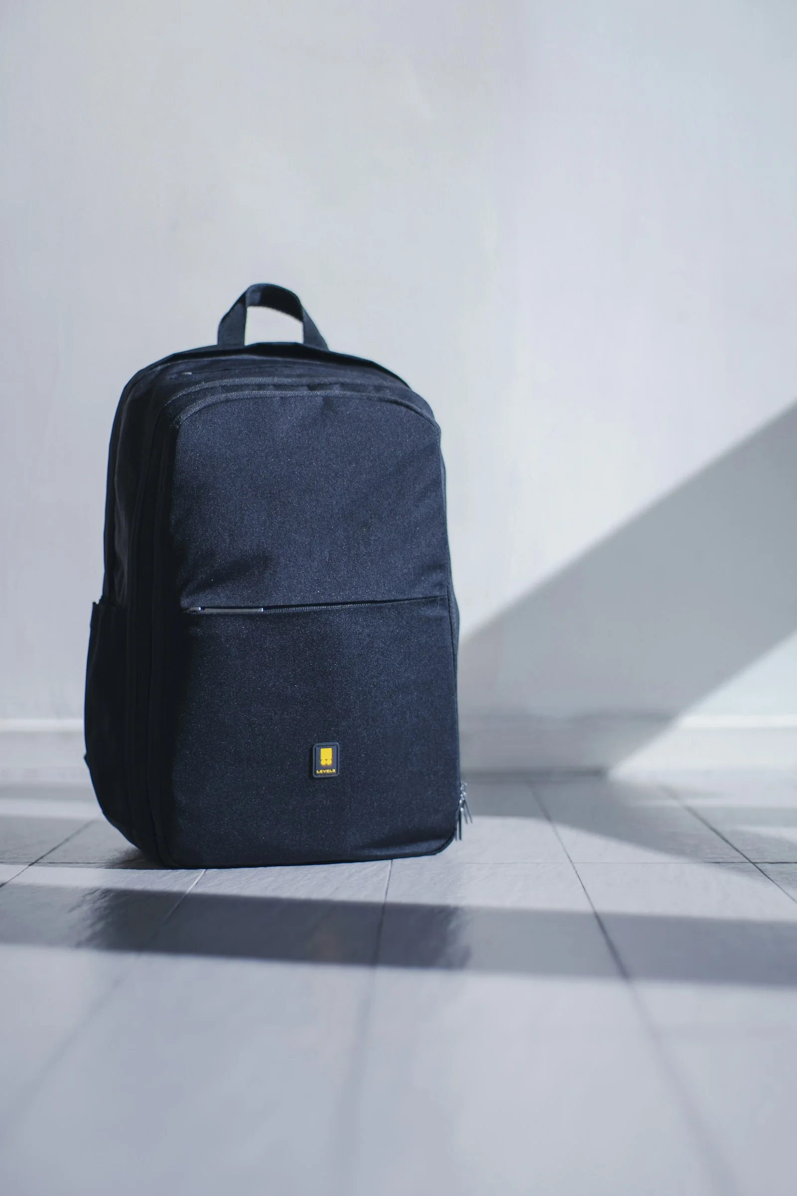 Black backpack against a pale wall.