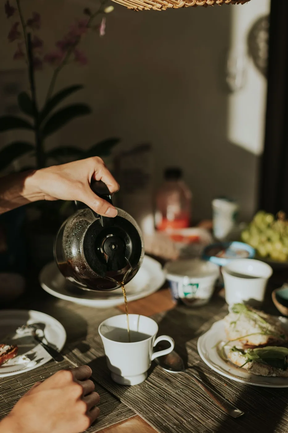 Coffee being poured at a table with cups and breakfast food.