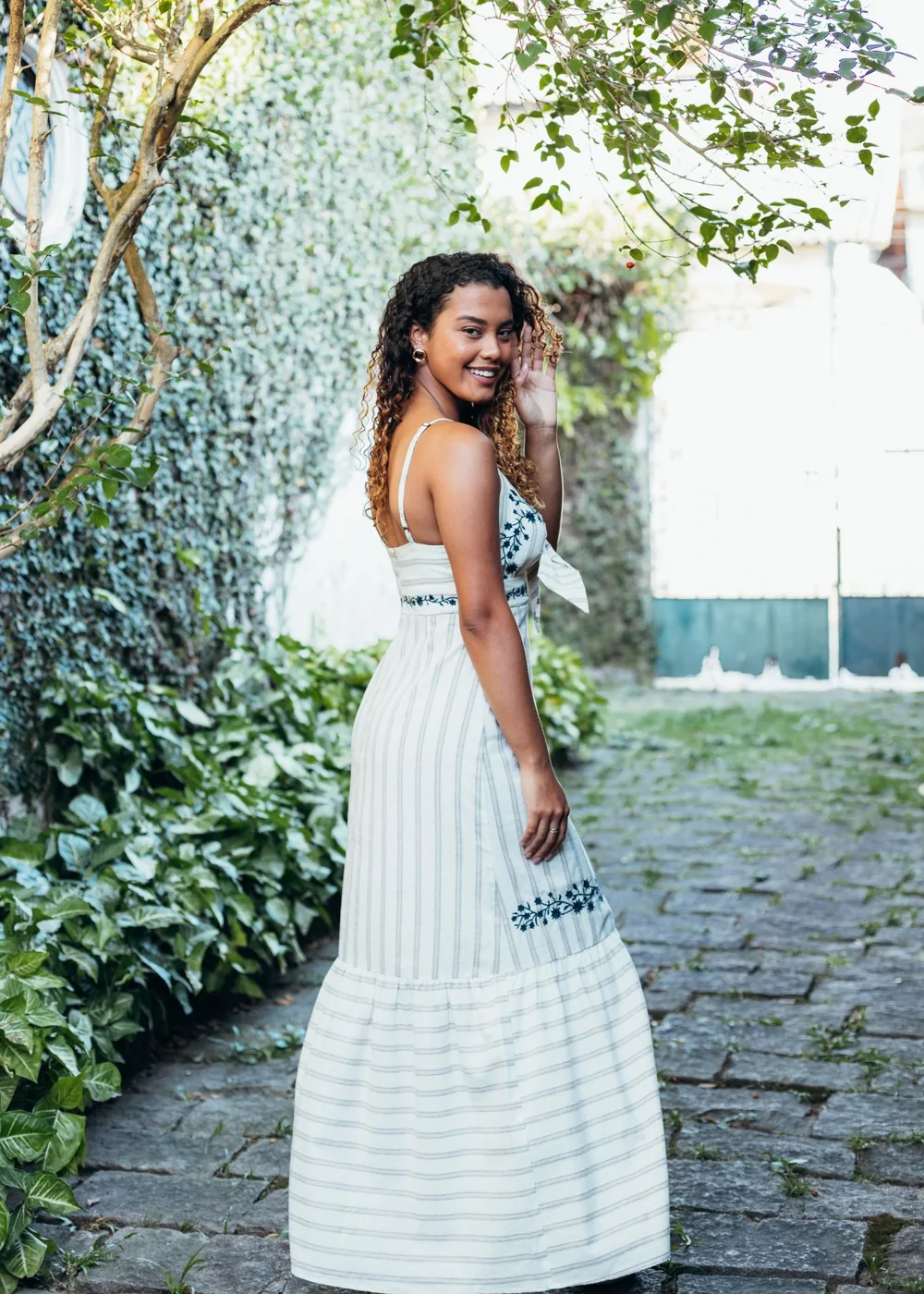 A woman wearing a pale dress with a small dark embroidered detail outdoors