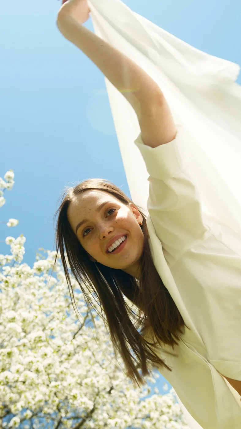 Woman in a white dress outdoors beside flowering trees