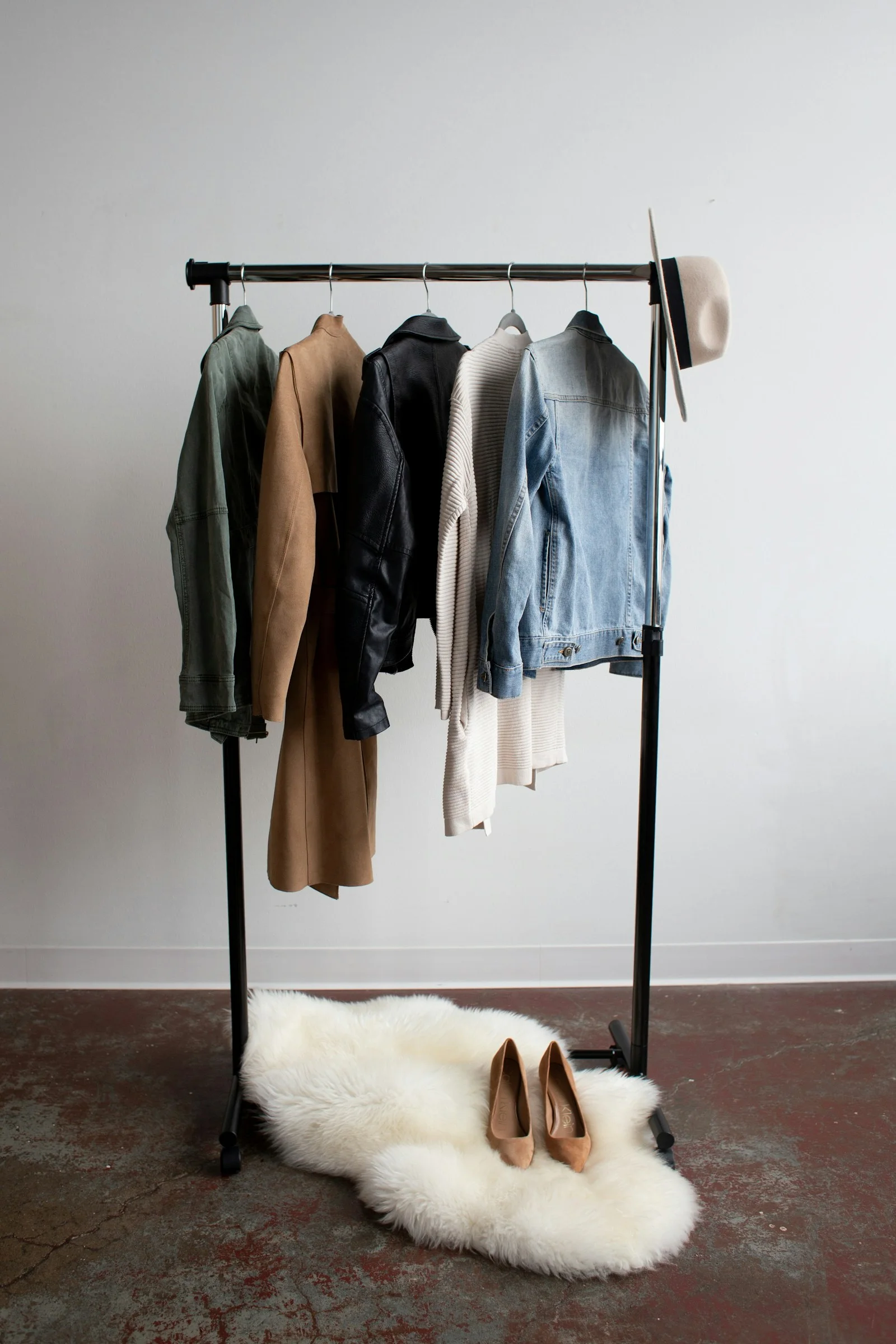 Clothing rail with coats and light garments above a rug.