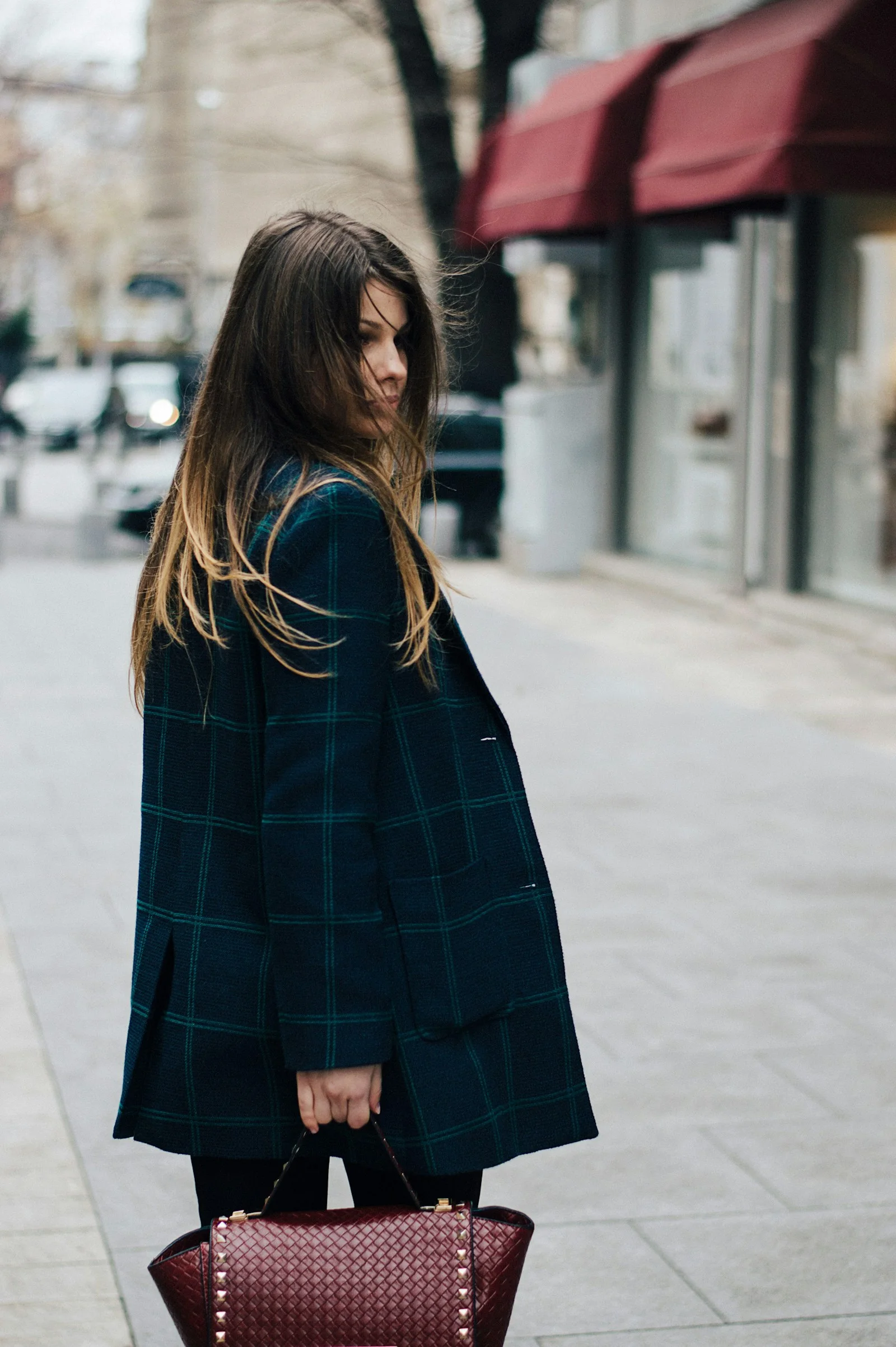 Woman in a dark coat carrying a structured handbag on a city pavement.