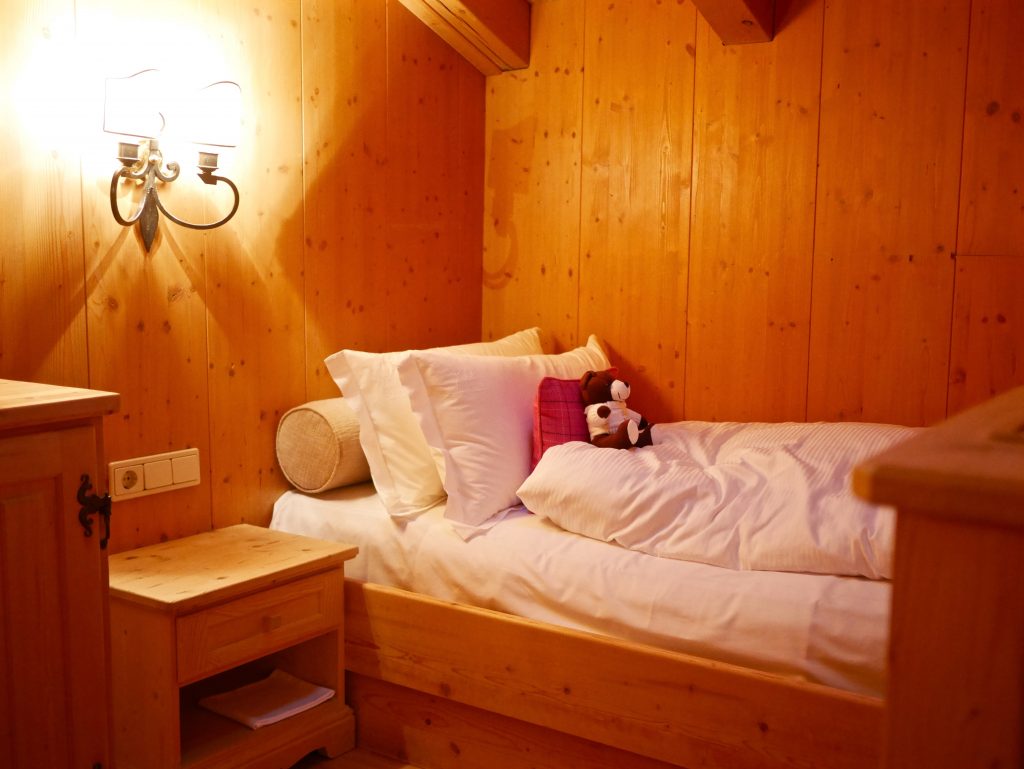 view of a single bedroom with wooden walls and teddy bear on the bed