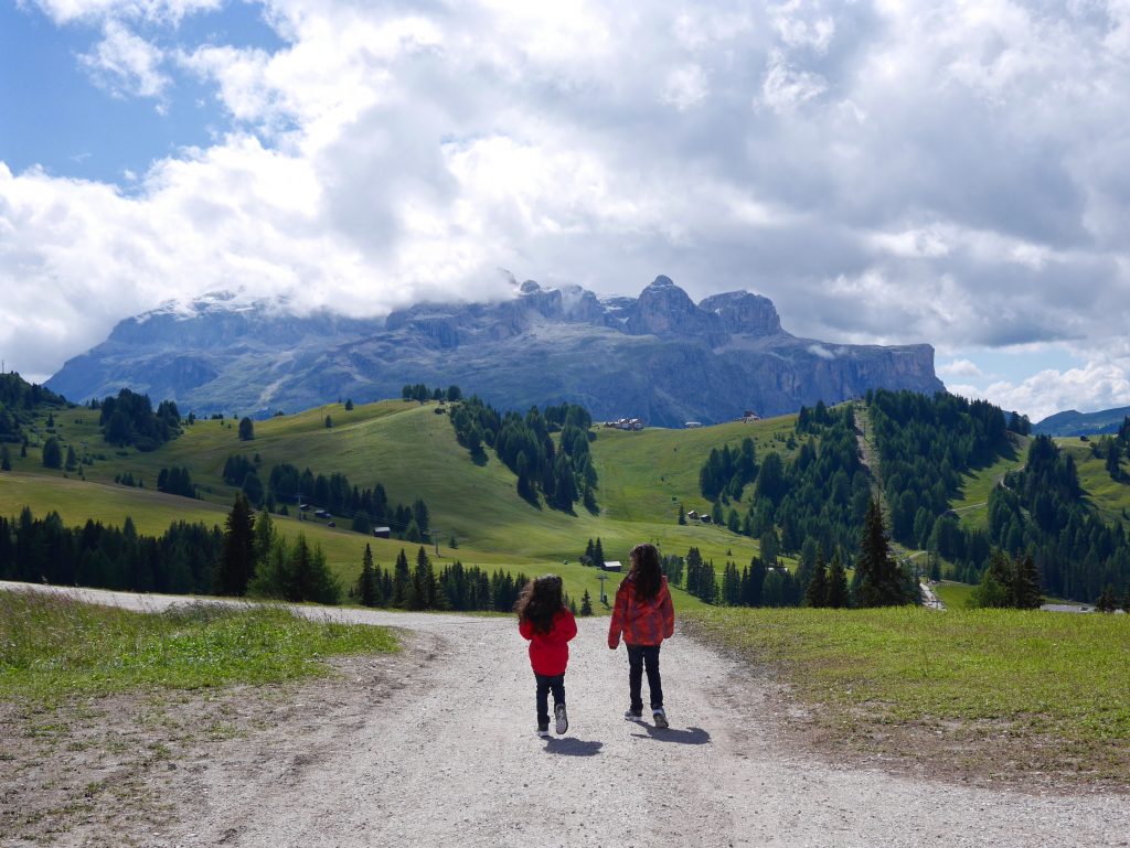 two girls in red jackets walking down the gravel path surrounded by greenery, hills and mountains