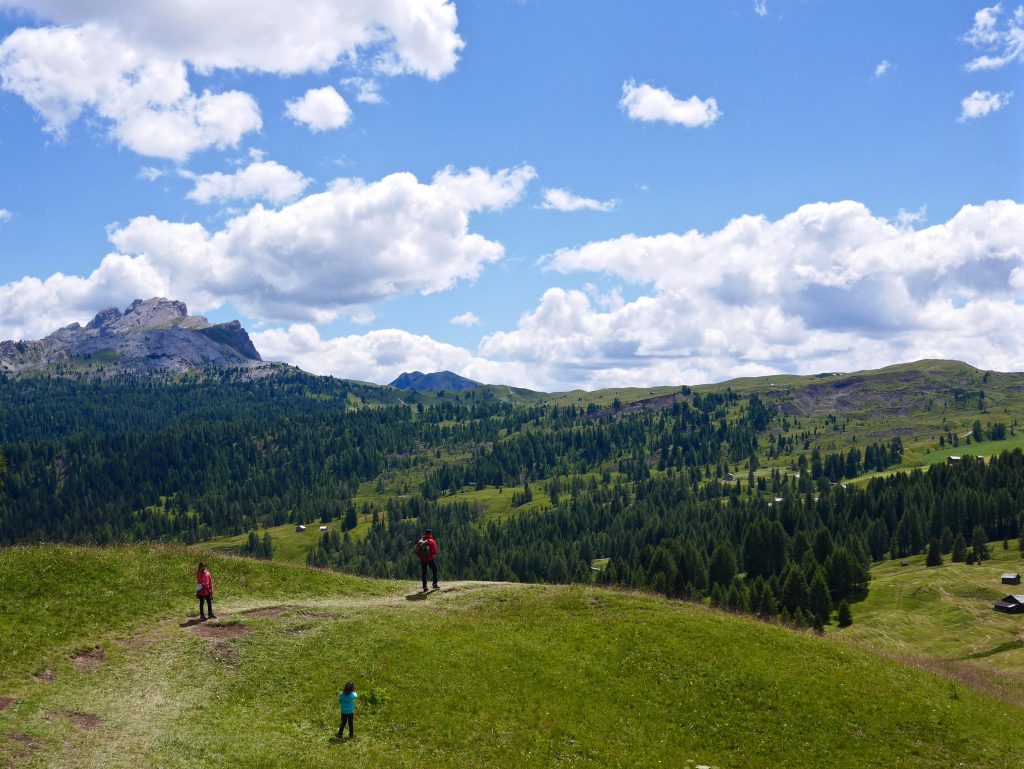 three people on a grassed hill looking over an Ariel view of the Italian Dolomites