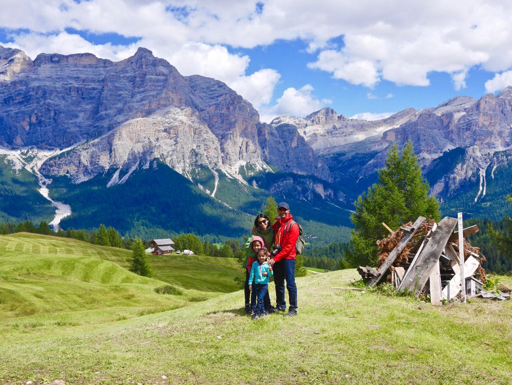 sima with family alongside a pile of wood overlooking valley and Dolomite mountains