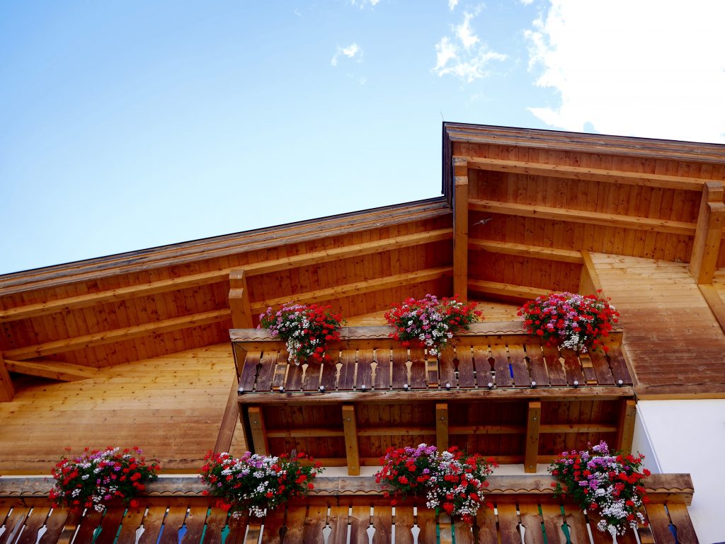 View of a wooden home with red, pink and white flowers/baskets decorating the balconies