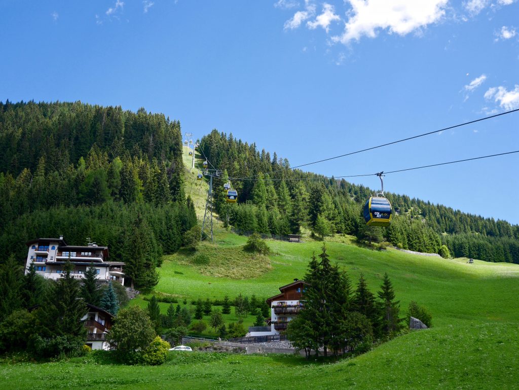 view of the cable cars taking people up the mountain alongside wooden resorts and pine trees