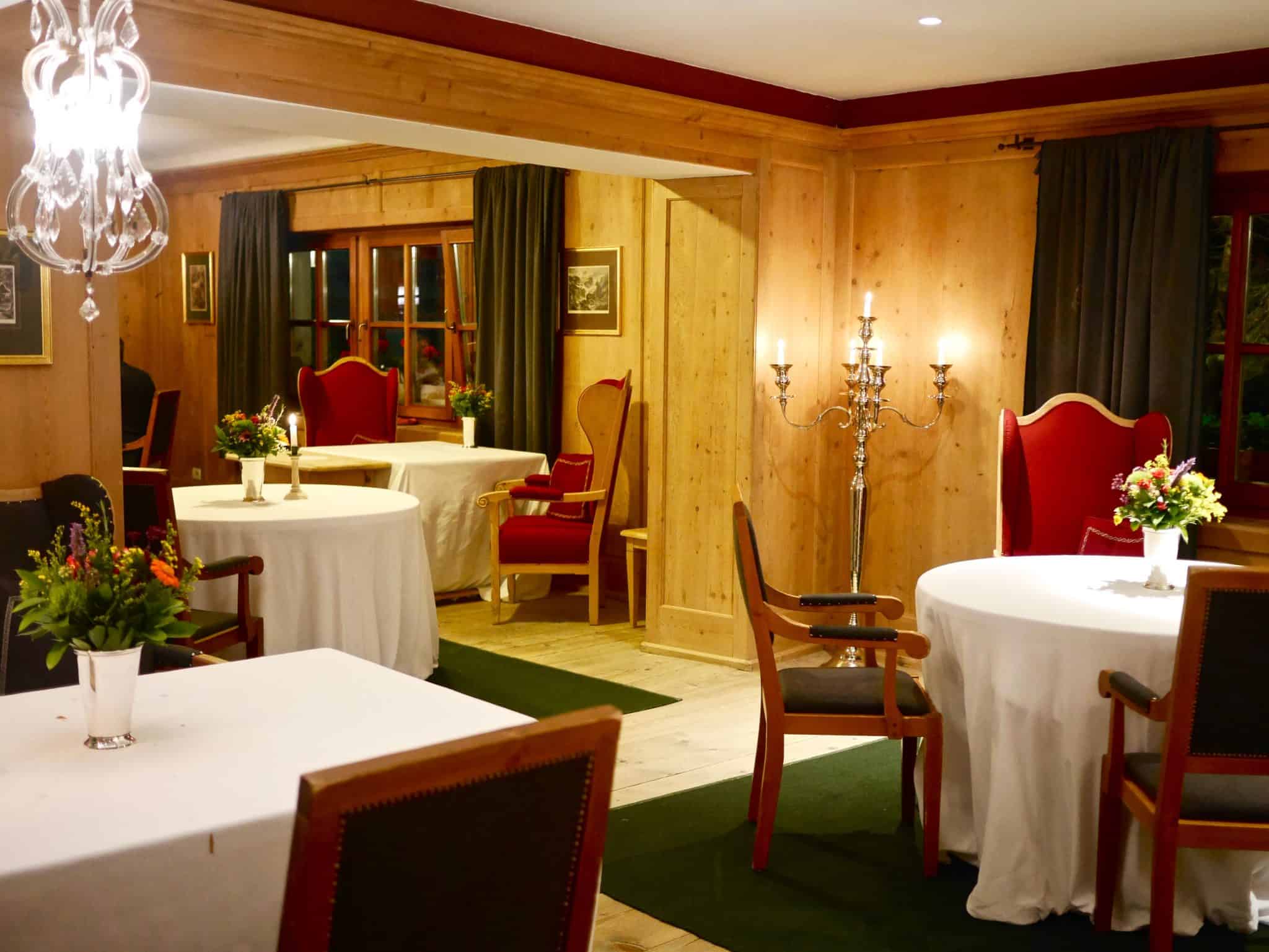 natural alpine surroundings, floor standing chandelier and red chairs with green rug and white table clothes