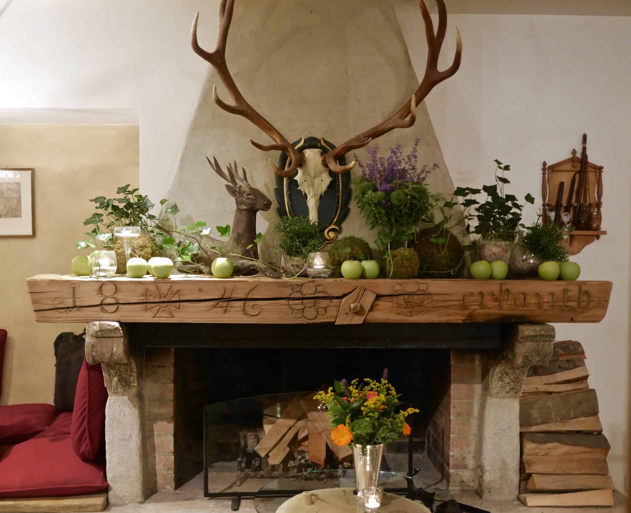 Fresh flowers, antlers surrounding fireplace with carvings and apples on top of mantle