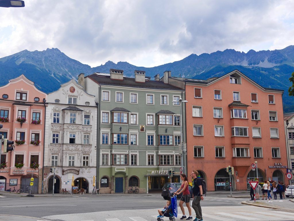 more buildings in old town painted pink, white, green and terracotta with rectangular windows with Innsbruck mountain tops above