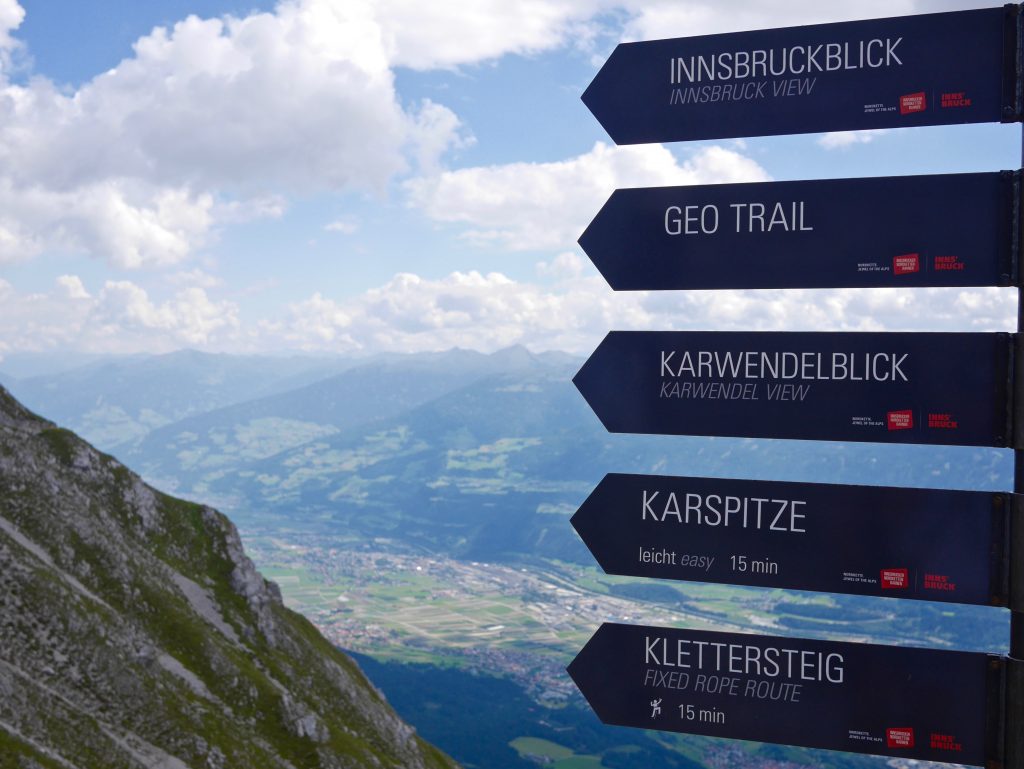 sign pointing towards  innsbruck view, geo train, karwendel view, karspitze and klettersteig with the mountain and innsbruck in the background