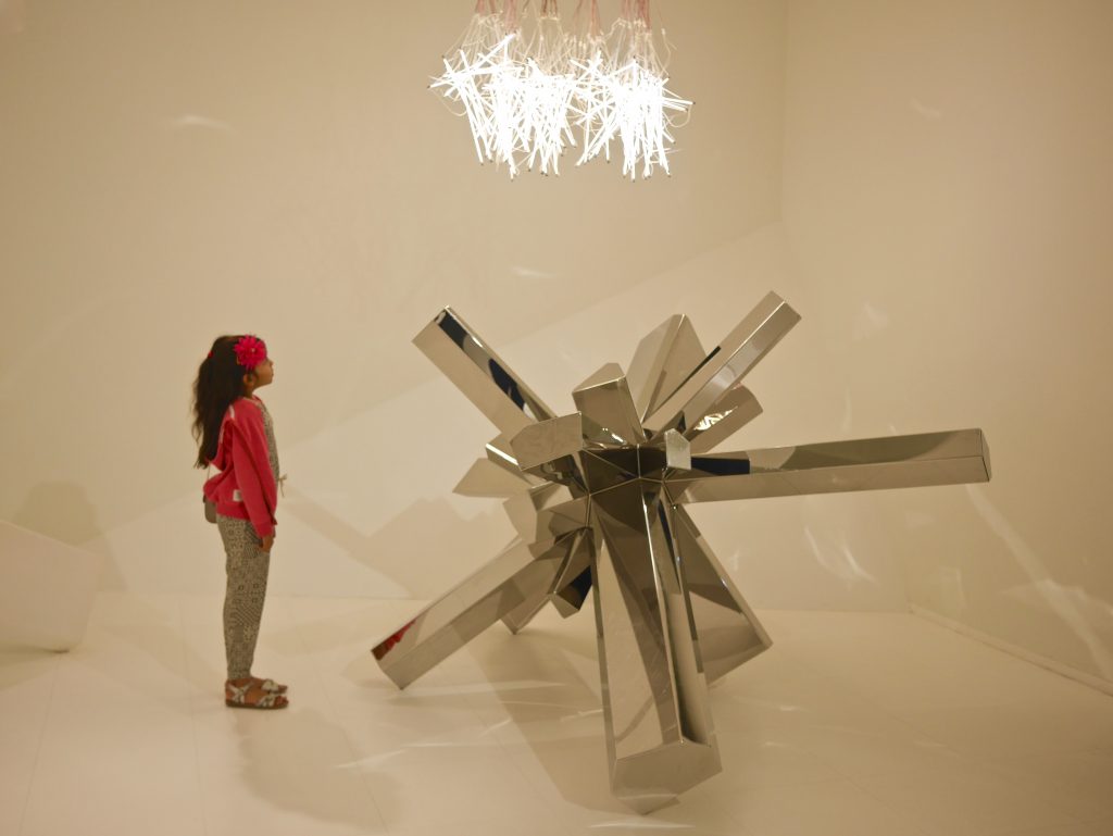 girl in red stood beside crystal through the use of glass, marble, steel and synthetic 3D prints.