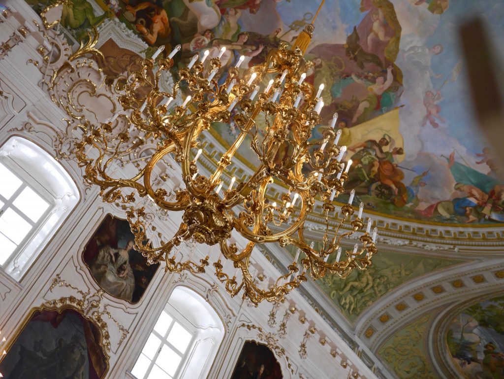 inside the Hofburg palace looking up at a gold chandelier and painted ceilings