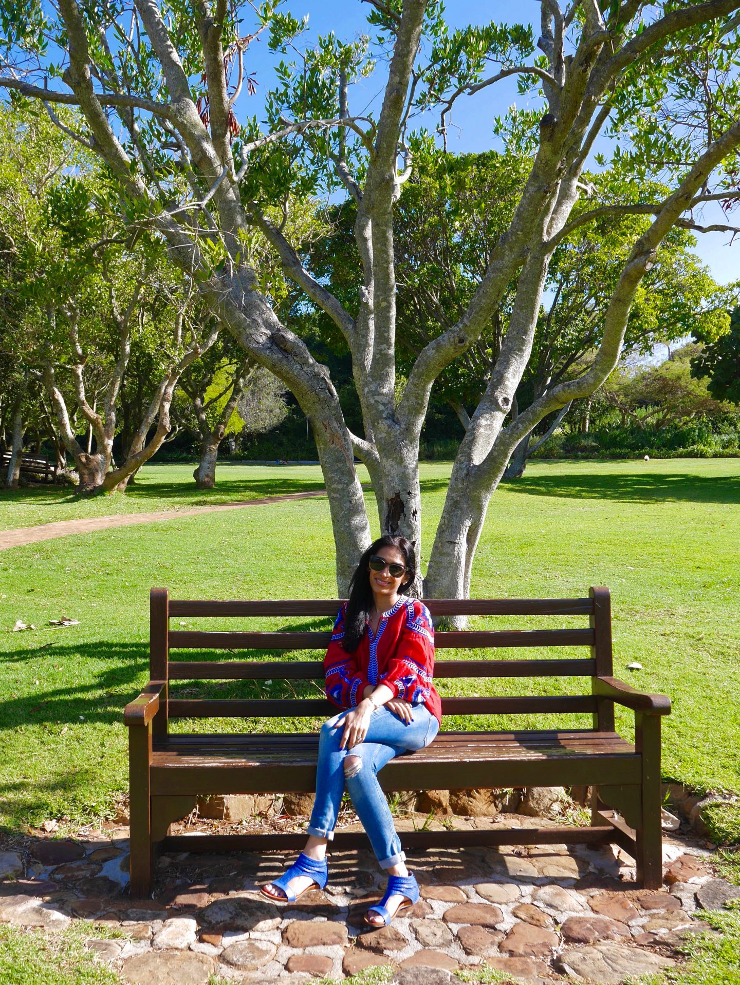 sima sat on a bench wearing blue shoes and a red kaftan in the botanical gardens