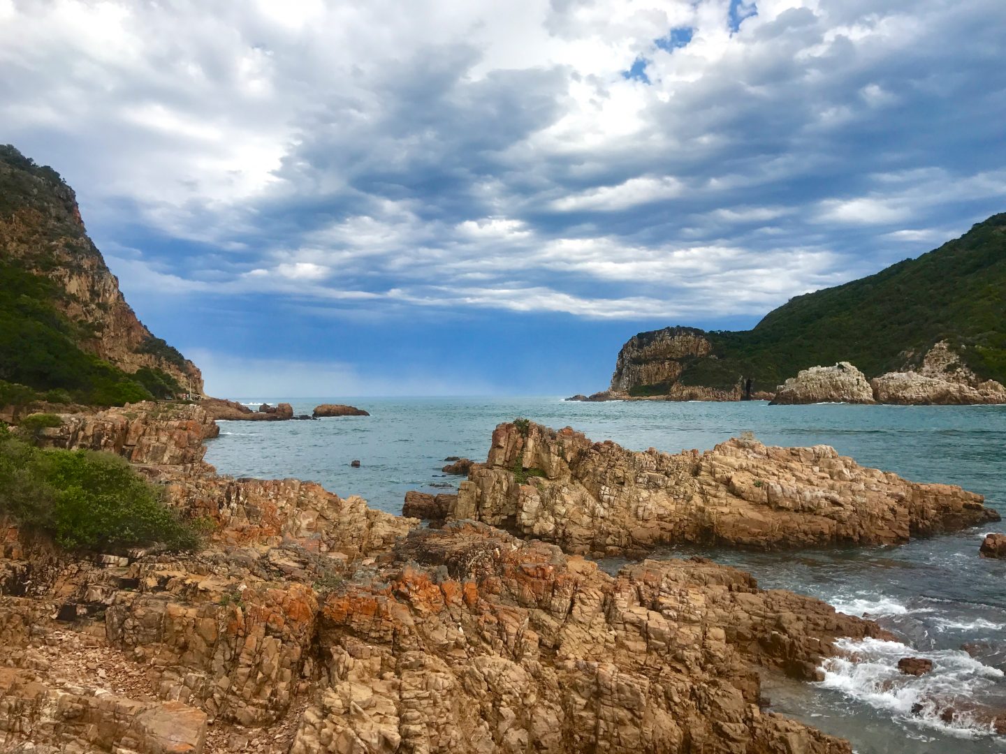 picture of brown rocks looking out to the Knysna Lagoon surrounded by tall green covered cliffs