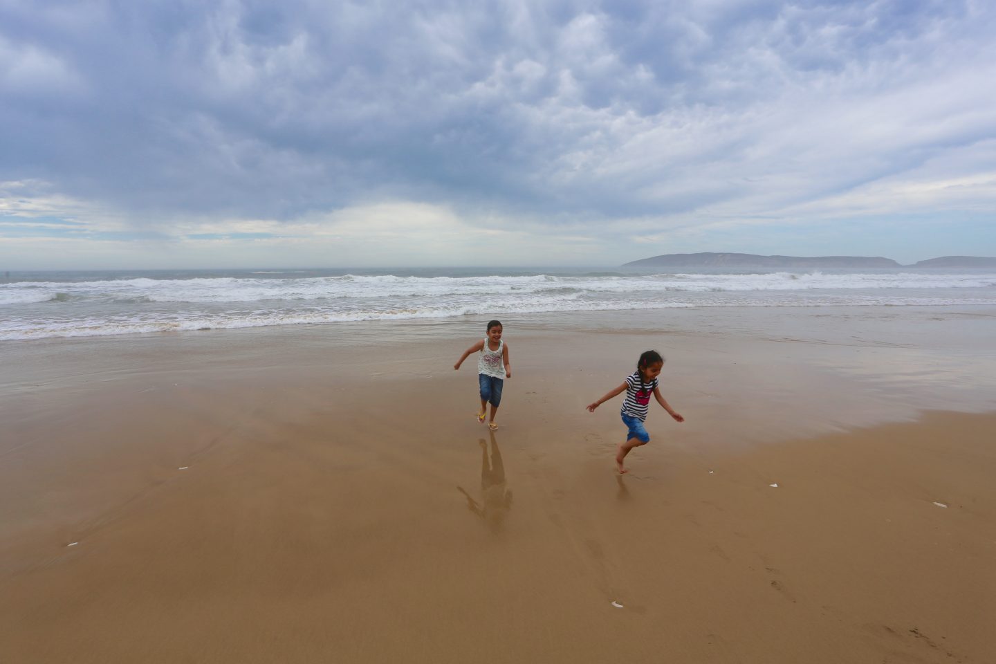 two girls wearing cropped jeans and t-shirts running on the stone free beach/sand of Plettenberg Bay