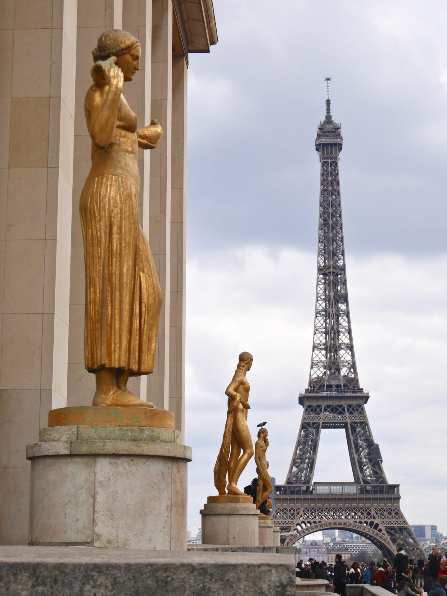 view of the effel tower with gold statues in the forefront of the picture