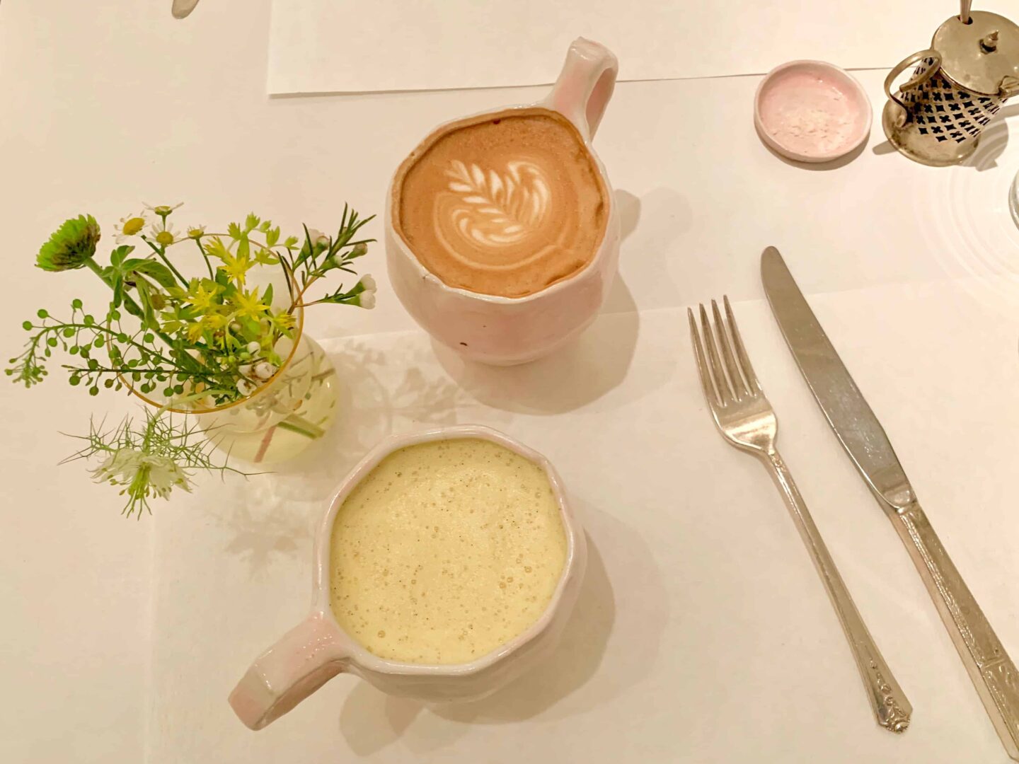 Flat lay of flowers in a vase, two drinks and knife and fork