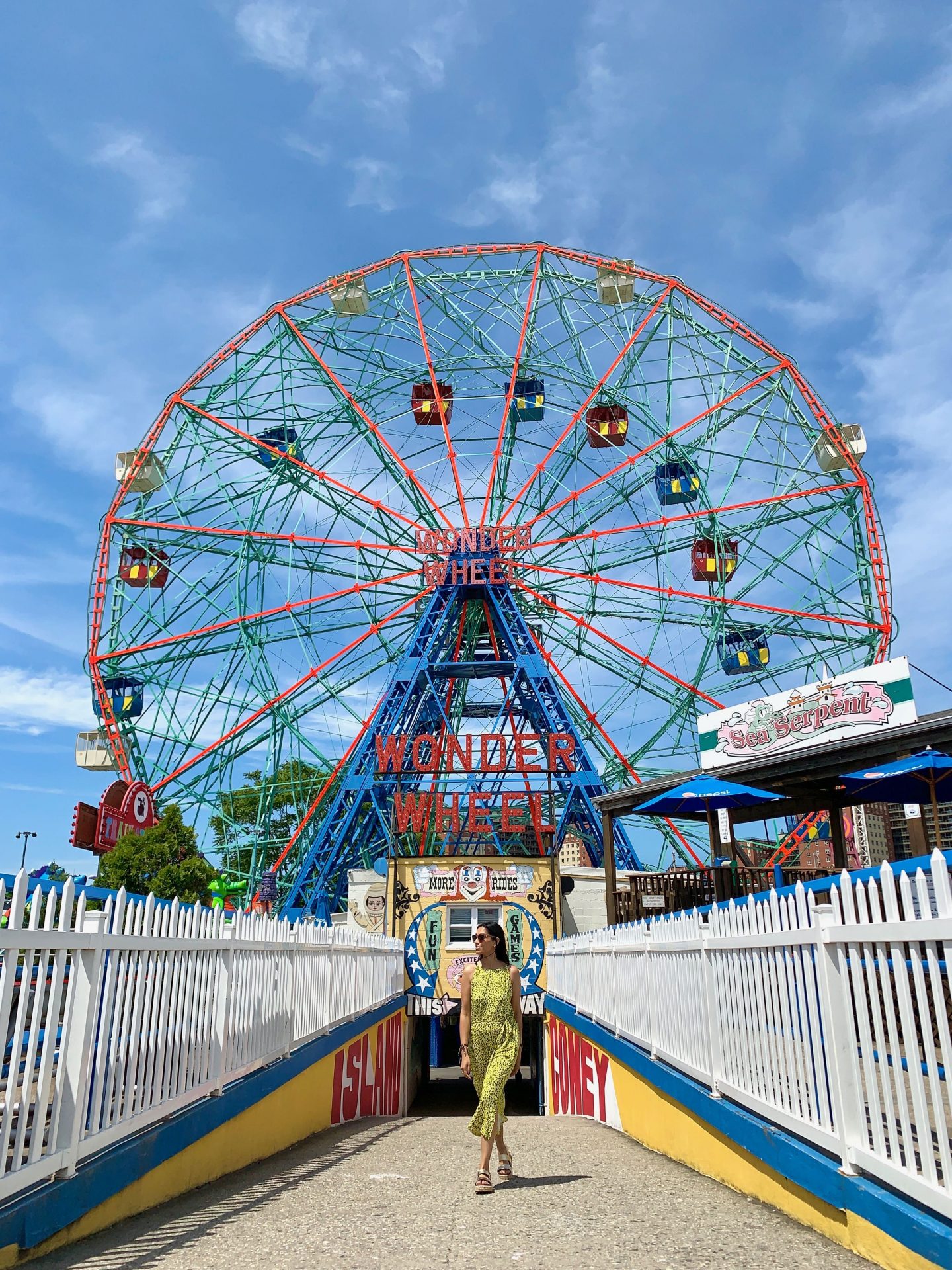 Sima in yellow jumpsuit beneath Blue, Red and Greem Wonder Wheel at Coney Island