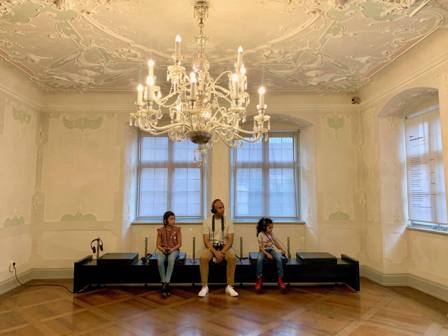 father and daughters listening to earphones under chandelier | Germany with kids