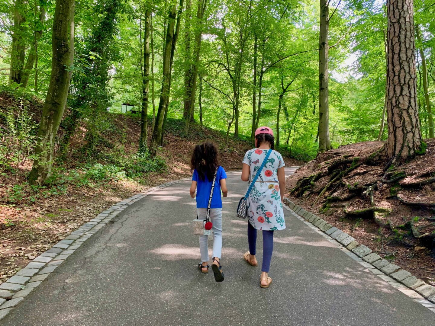 two girls walking away from camera along path in the wooded park at Nuremberg Zoo | Germany with kids