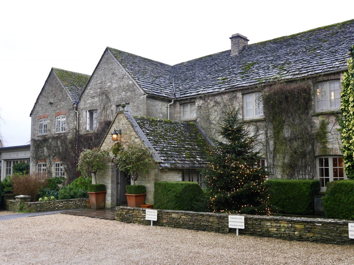 image of the outside of Calcot Hotel & Spa in The Cotswolds with a christmas tree, shrubbery and parking spaces out the front in