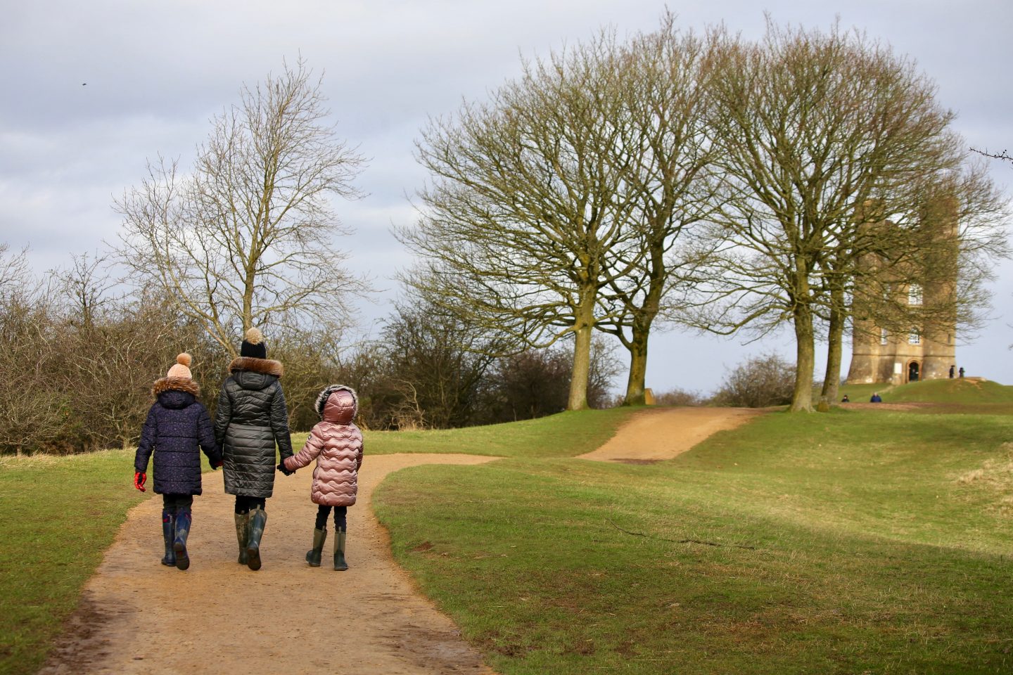 picture of three girls walking along a sanded path towards a tall tower in The Cotswolds