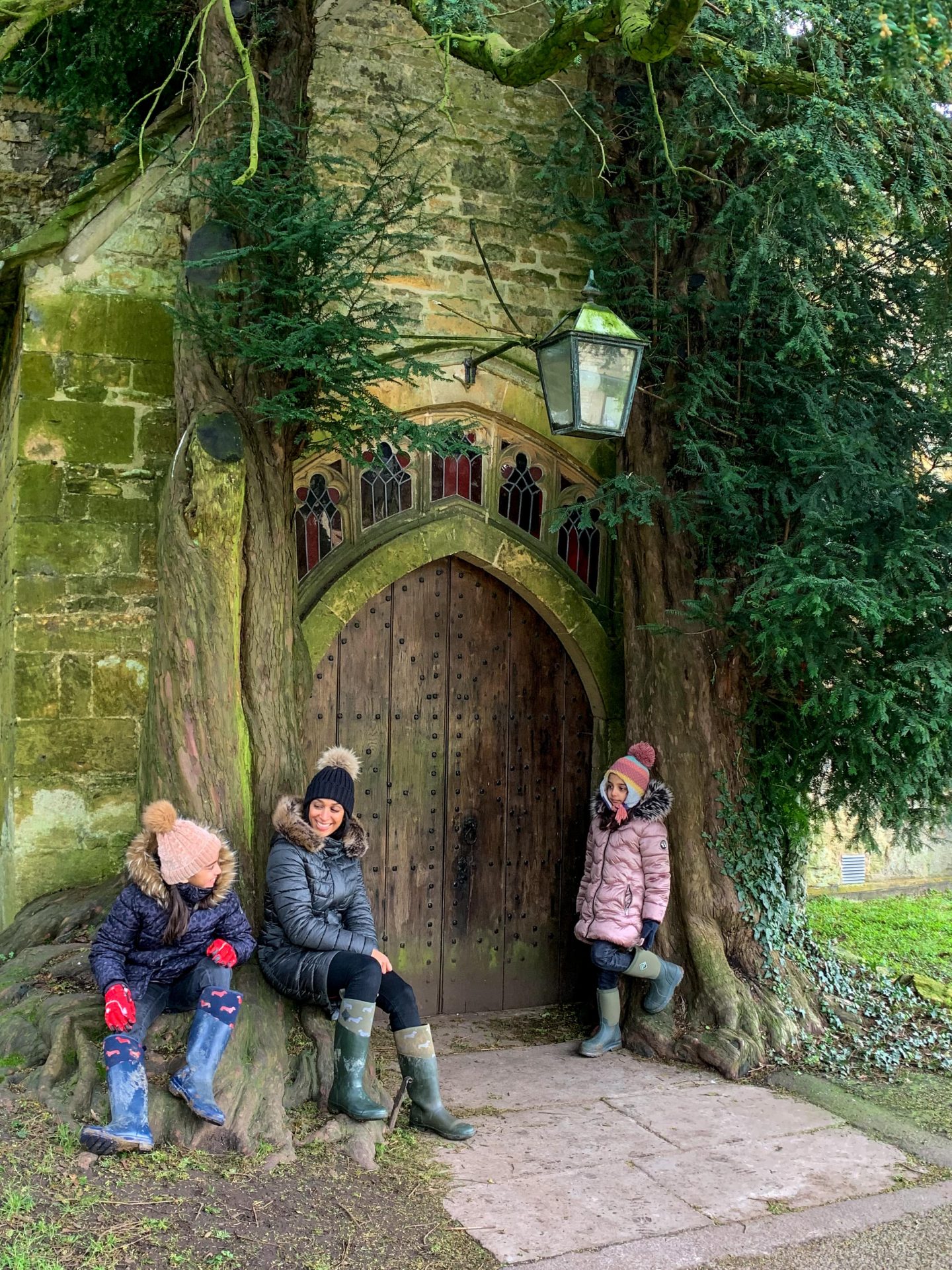 family sat on the bottom of a treee trunk outside the doorway of st Edwards church