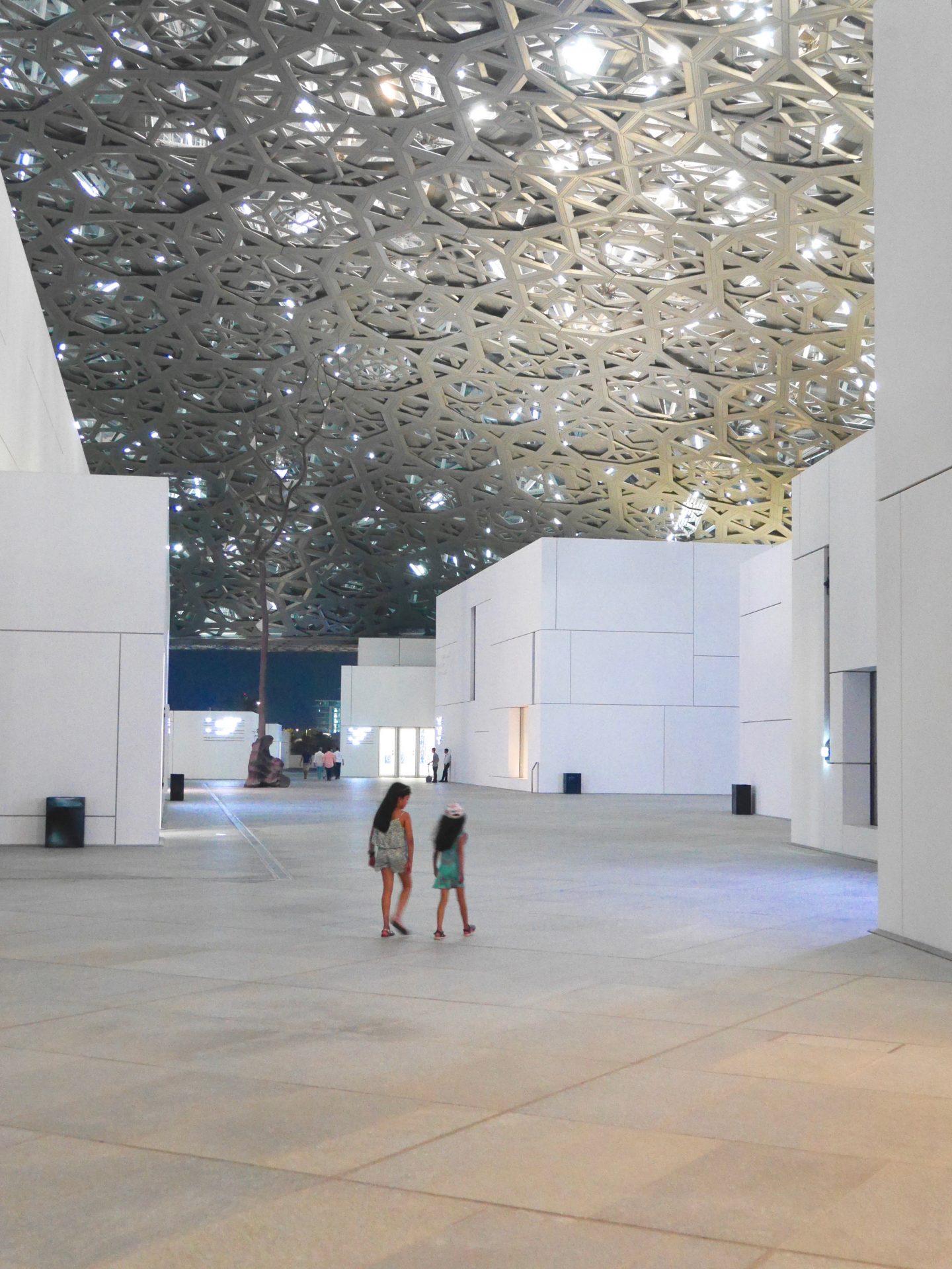 image of two girls walking through the stone floors and metal crafted ceiling in the the Lourve Abu Dhabi 