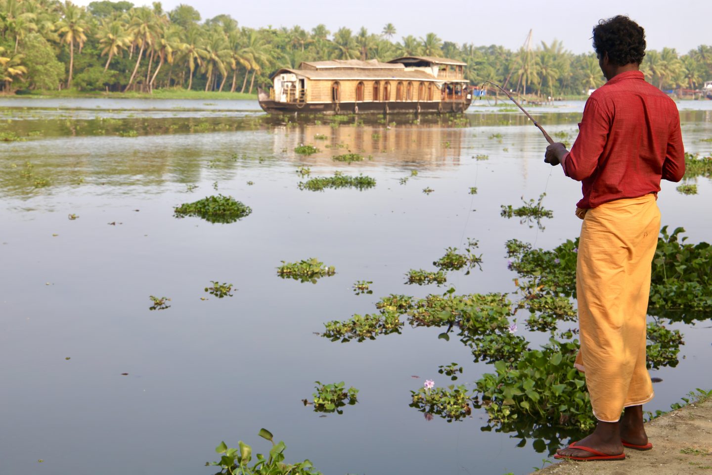 gentleman in yellow trousers and red shirt fishing looking over a river in kerala 