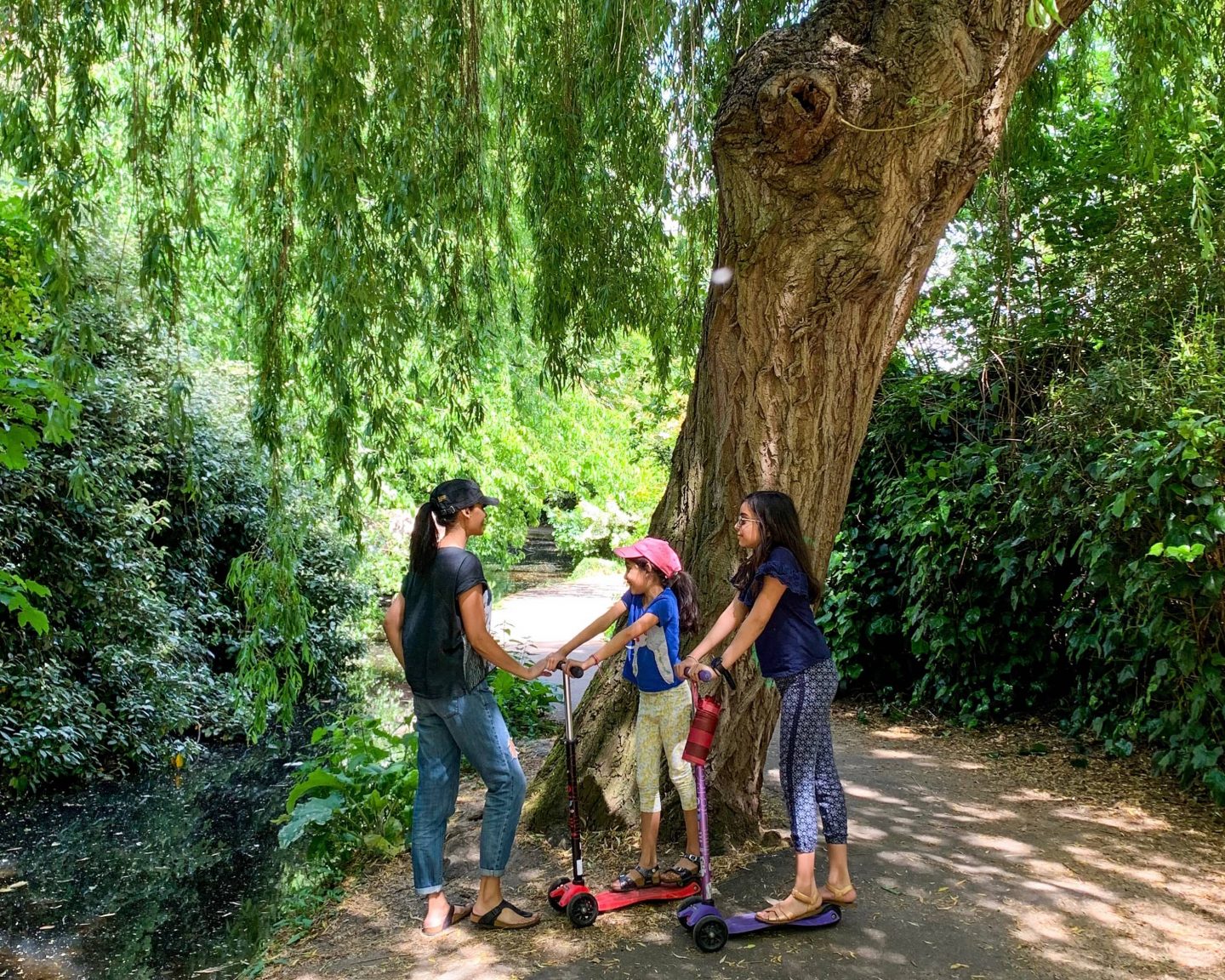 image of sima and two children on blue and red scooters under the tree on the new river walk