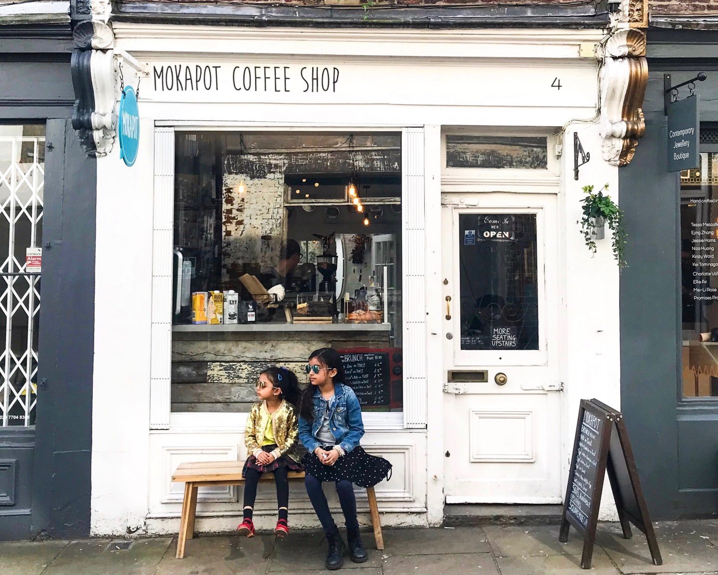image of two girls wearing sunglasses outside on a bench in front of the window of MokaPot Coffee Shop
