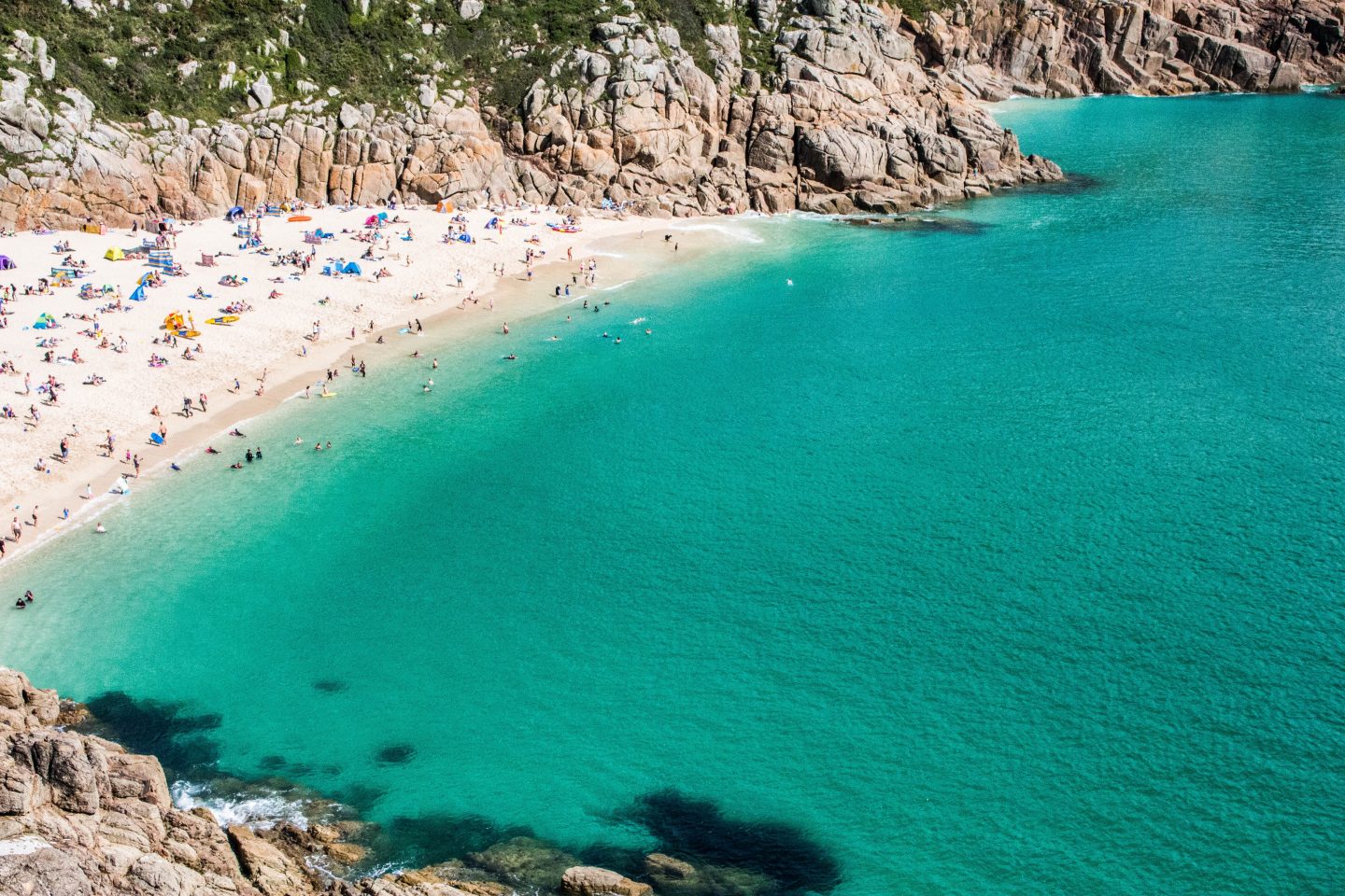 view of Porthcurno beach cove from the sky or a high cliff looking over people on the beach and blue green sea