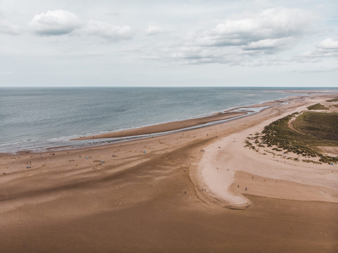 view of holkham beach from the air with beach for miles, small lakes and green trees