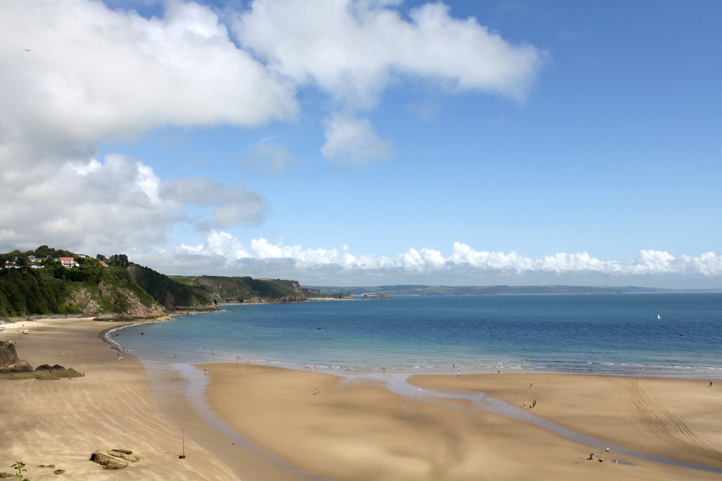 view of a beach from a cliff top overlooking the blue sea and sand