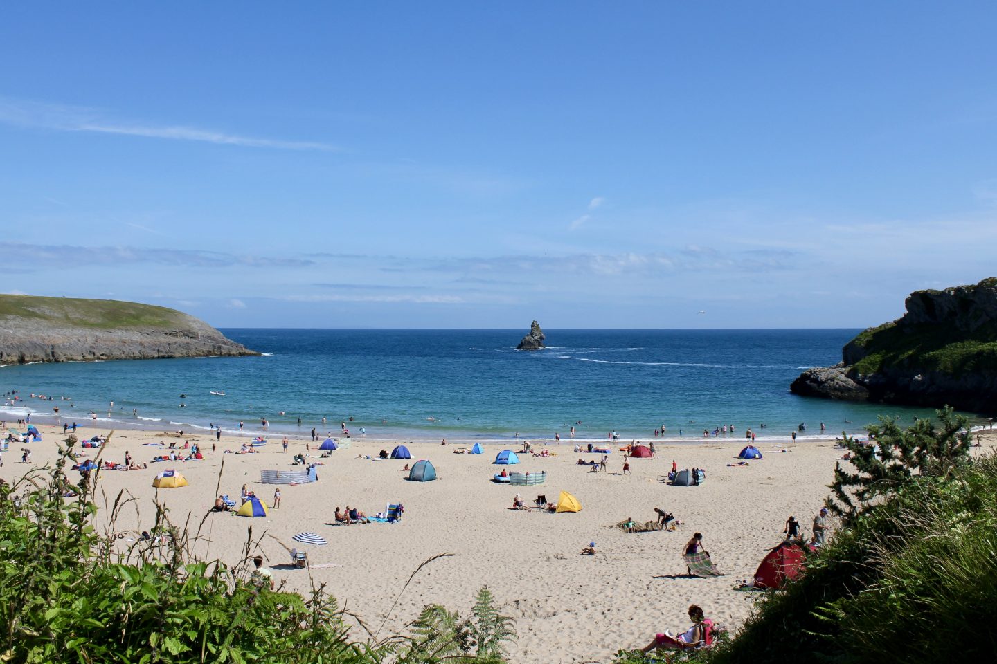 view looking towards the seat on Broad Haven South beach with people, sun shields, brolly and blue sea surrounded by cliffs