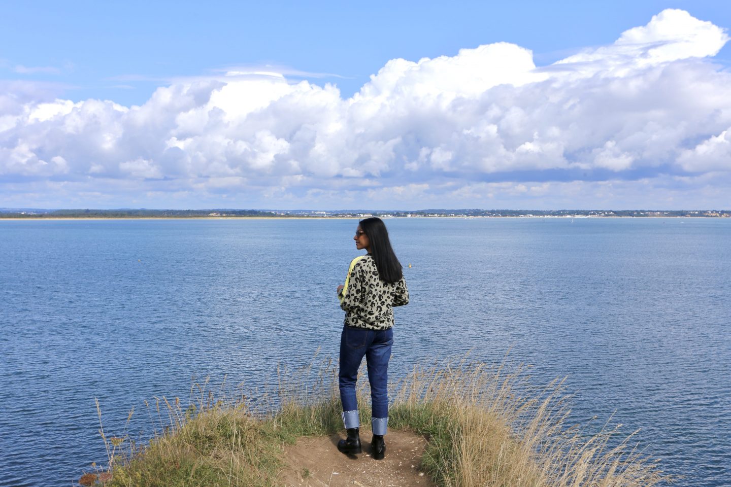 sima wearing jeans and grey and yellow top overlooking the sea from a cliff top
