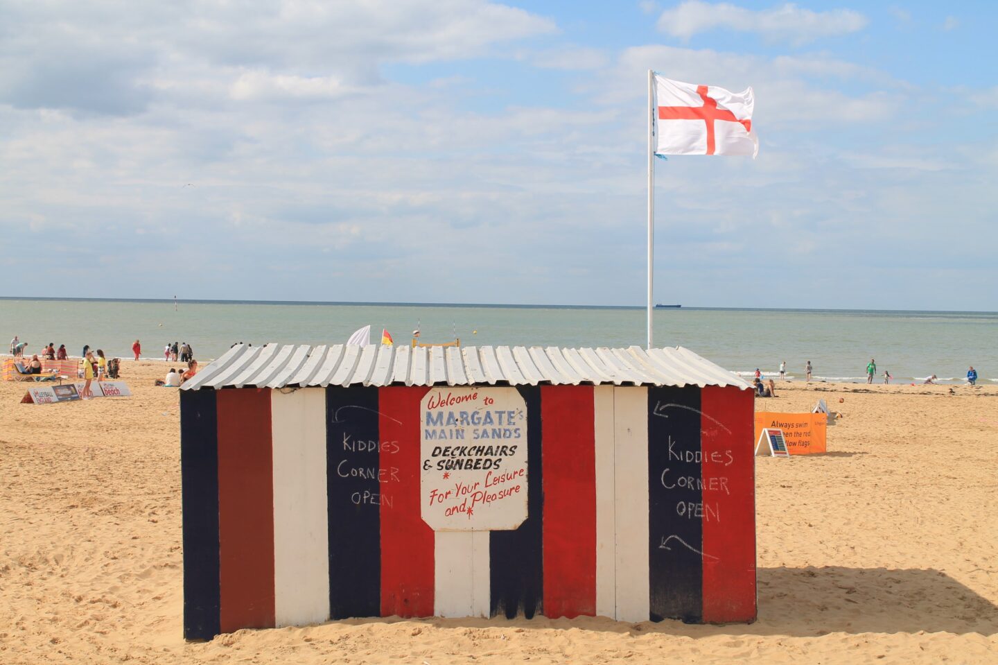 view of a blue, red and white striped deckchair and sunbed hut on the beach