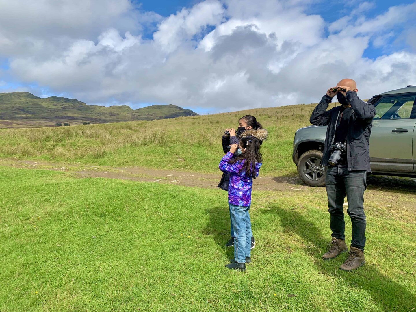 two girls and father looking through binocular across the highlands