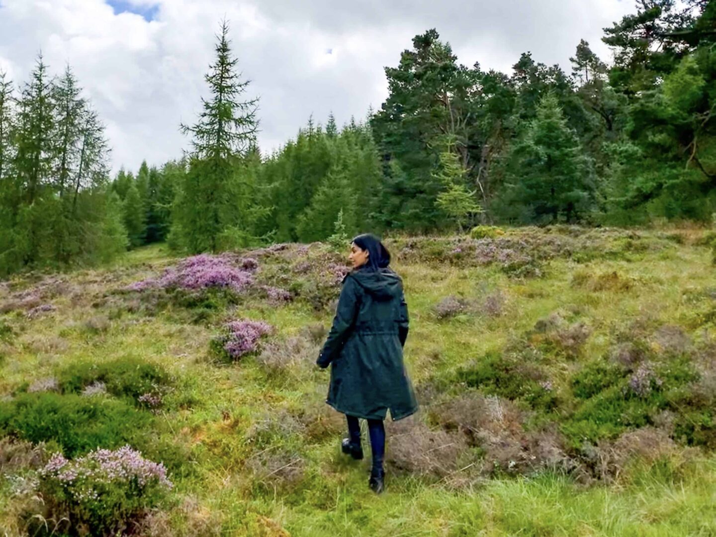 sima wearing a dark blue coat walking through the fields of the highlands