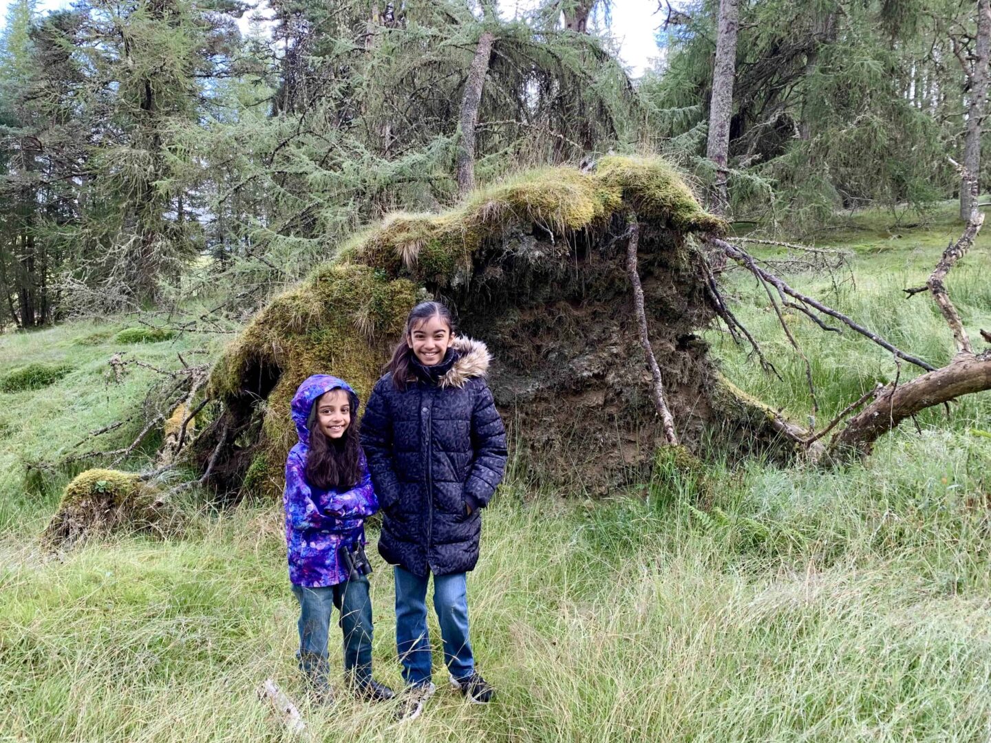 view of two girls in front of a uprooted tree