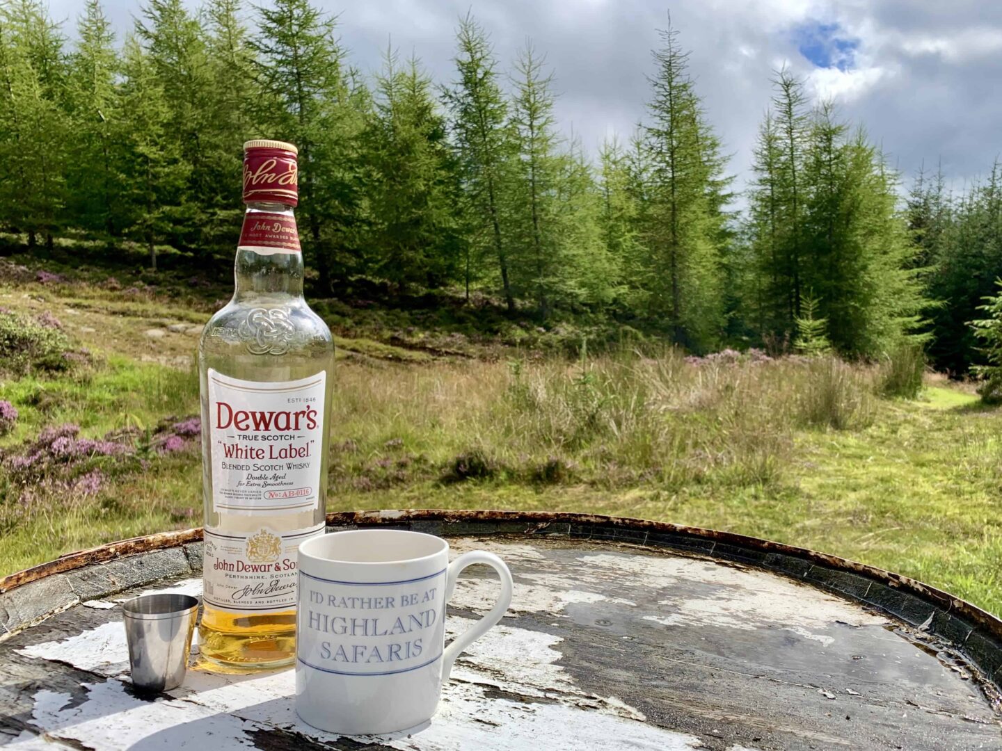 view of dewars white label scotch whisky and a mug saying 'id rather be at highland safaris'