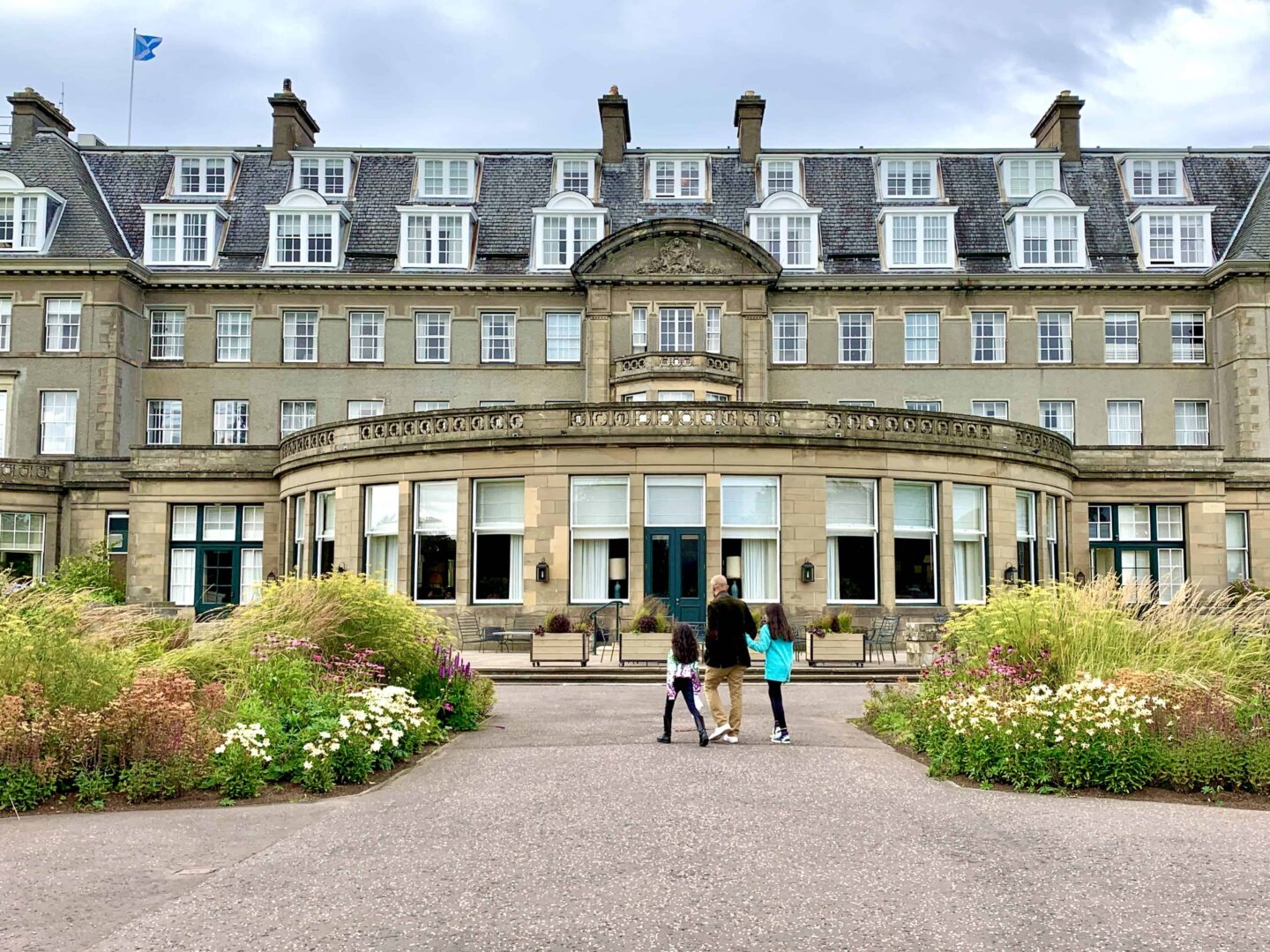 view of the front of Gleneagles hotel with two children and father holding hands walking towards the entrance