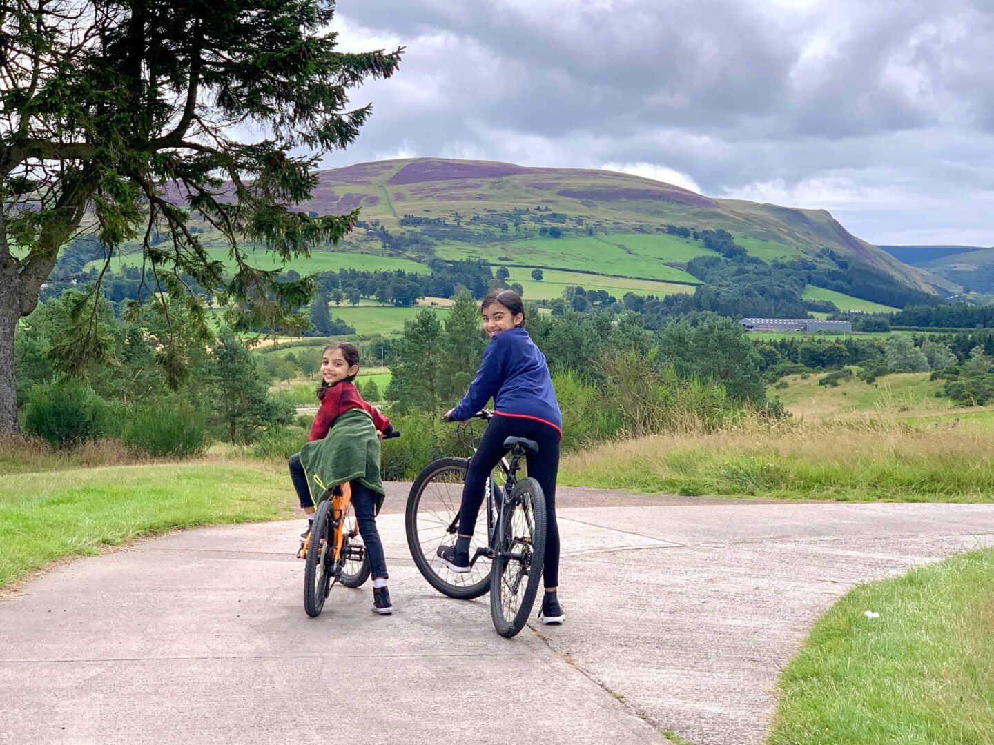 view of Simas children one wearing red on an orange bike and one wearing blue on a black bike overlooking the views of Ochil Hills