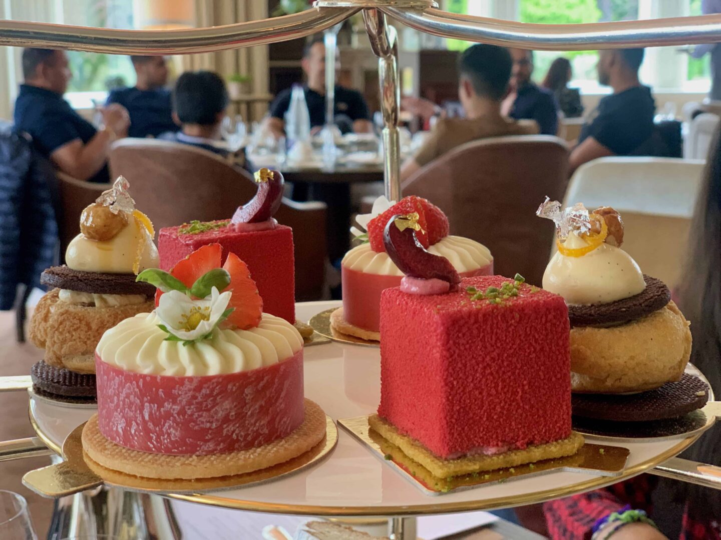 view of the colourful warm flaky scones, Valrhona chocolate, orange and praline choux and the most delicious morello cherry, pistachio gateau with vanilla sable on the layer of the afternoon tea cake stand